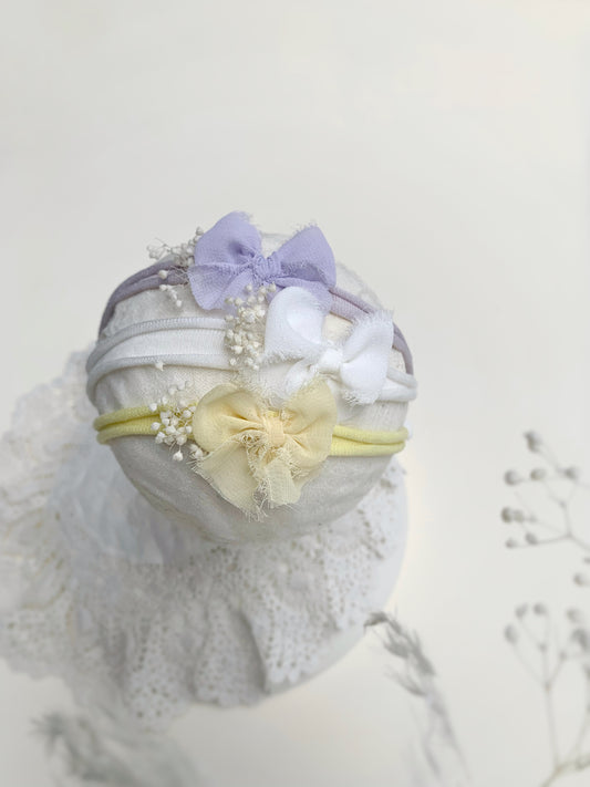Set of three pastel baby bow headbands lilac yellow and ivory on white background