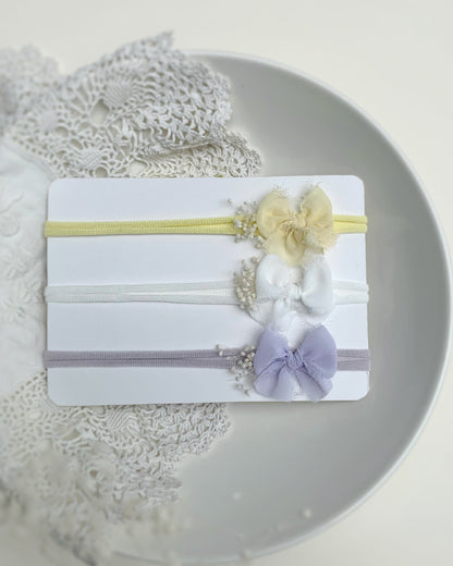 Set of three pastel baby bow headbands on a white card in  lilac yellow and ivory on white background