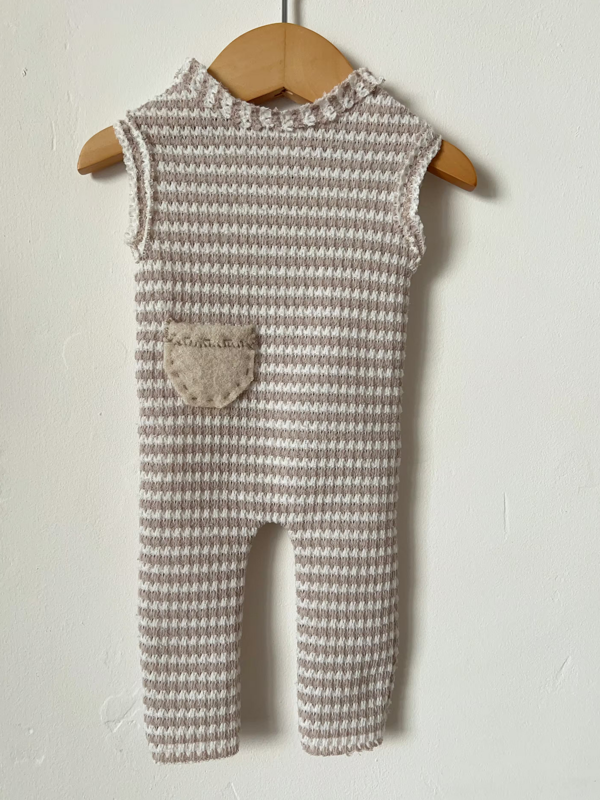 back of the beige newborn romper on a white wall
