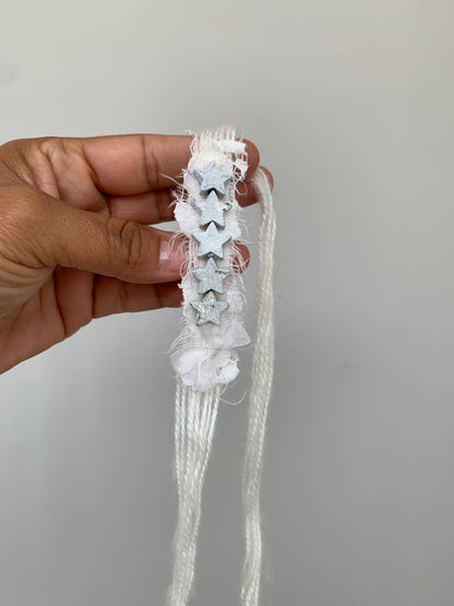 a hand holding a very delicate baby headband with little stars in silver grey and white