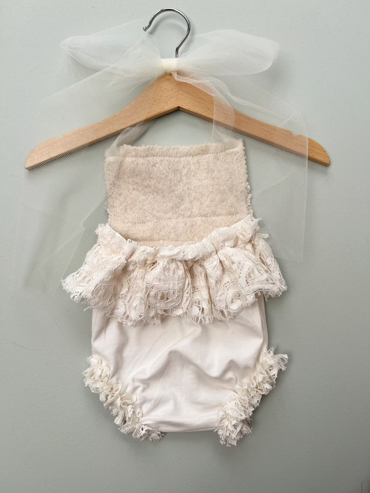 detail of the open back baby rompers on a wooden hunger and plain background
